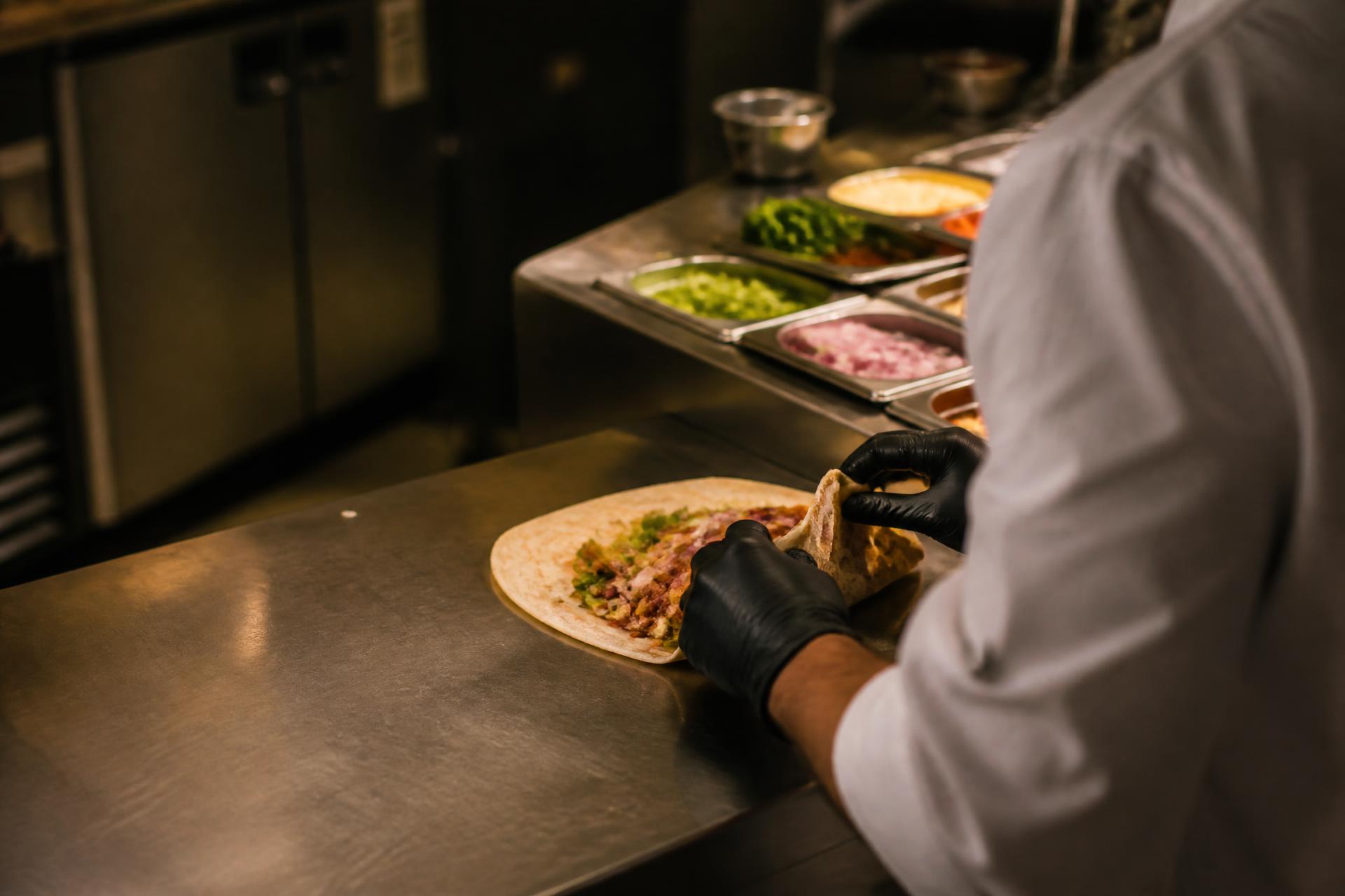 Chef hand-wrapping a fresh roll on a stainless steel counter in a modern kitchen